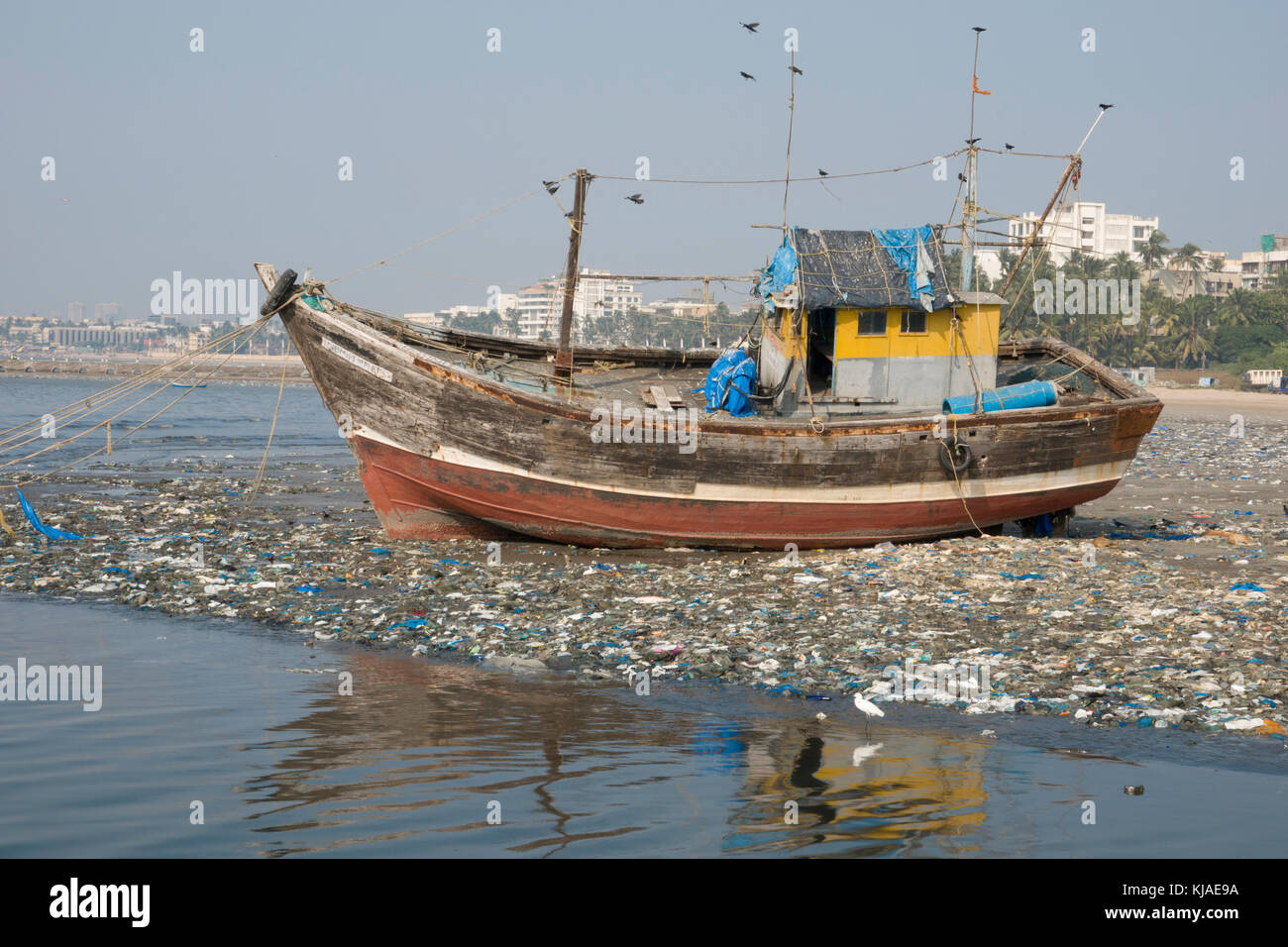 Barca di pesca in legno sulla spiaggia tra i rifiuti di plastica a Mumbai, India Foto Stock