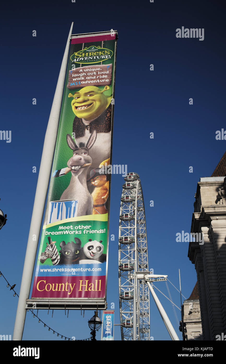 Un flag lampost banner pubblicitario su Southbank Londra Inghilterra pubblicità il Shrek avventura con il London Eye in background. Foto Stock