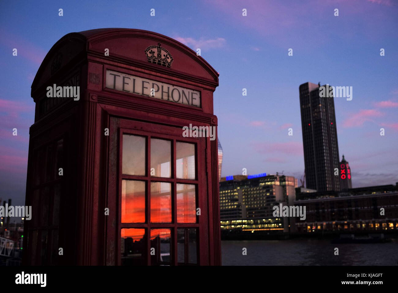 Inglese tradizionale telefono casella rossa a Londra con tramonto riflesso in Windows. Foto Stock