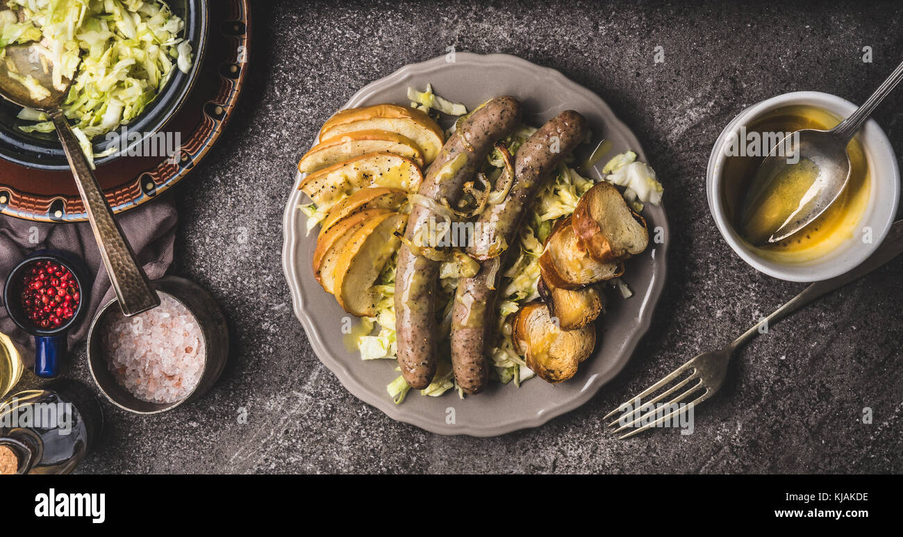 Salsicce fritte con mele cotte, cipolle e lye bun toast servita sul tavolo rustico con bianco insalata coleslaw e senape dip , piastre e forcella, top Foto Stock