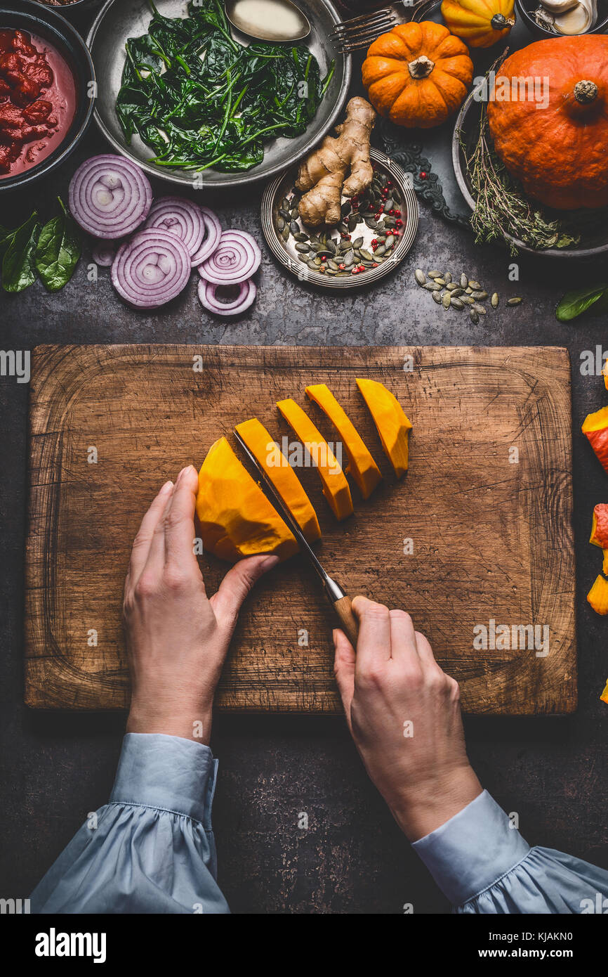 Donna femmina mani tagliare la zucca sul tagliere con coltello e varie verdure e condimenti per il gustoso piatto stagionale per la cottura, rustico Foto Stock