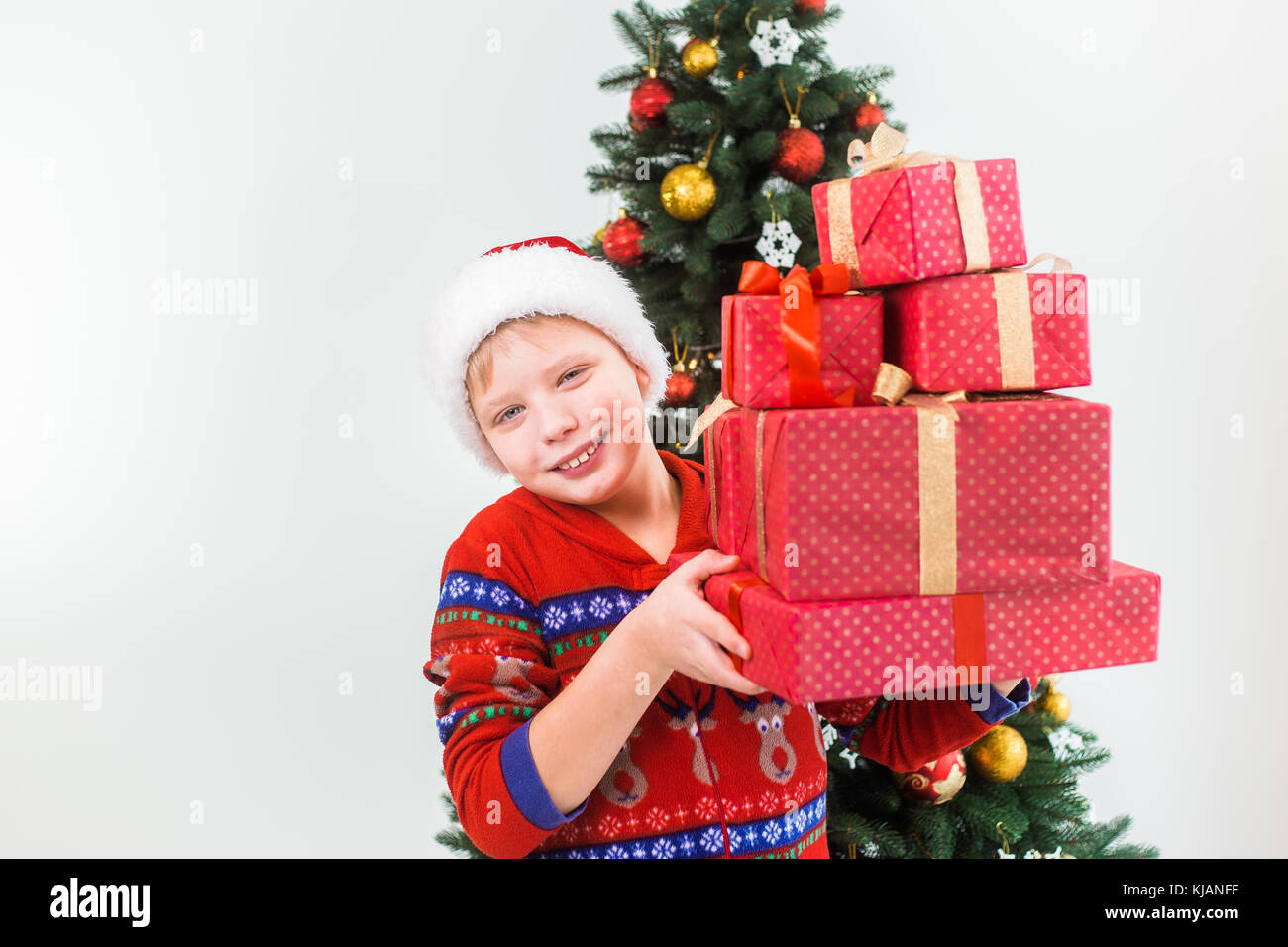 Closeup ritratto di sorridenti bambino holding pila di scatole presenti nelle mani pronta ad aprire loro. ragazzo indossa santa hat e pigiami rosso. vacanze gree Foto Stock