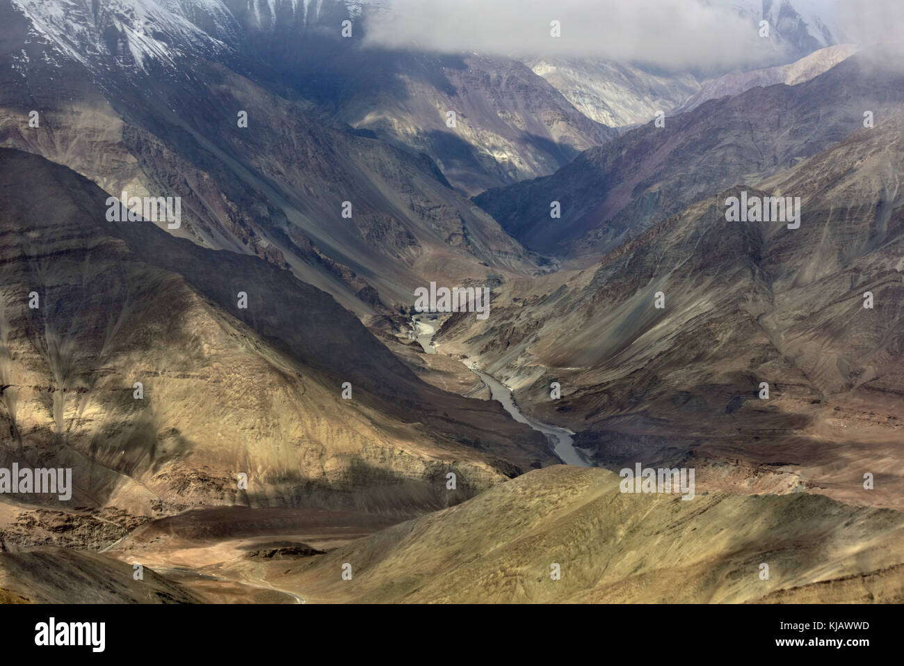 Valle di montagna: un burrone da alte montagne e il fiume è fangoso grigio sul fondo e le colline sono illuminate dal sole e coperto dalle nuvole, Foto Stock