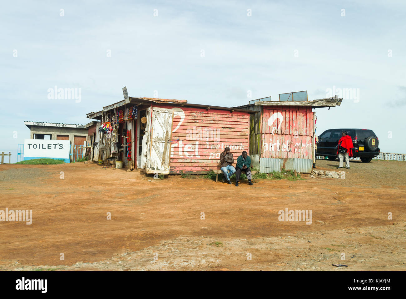 Un piccolo negozio di curiosita' fatta da lamiere grecate con persone seduto fuori, Kenya, Africa orientale Foto Stock