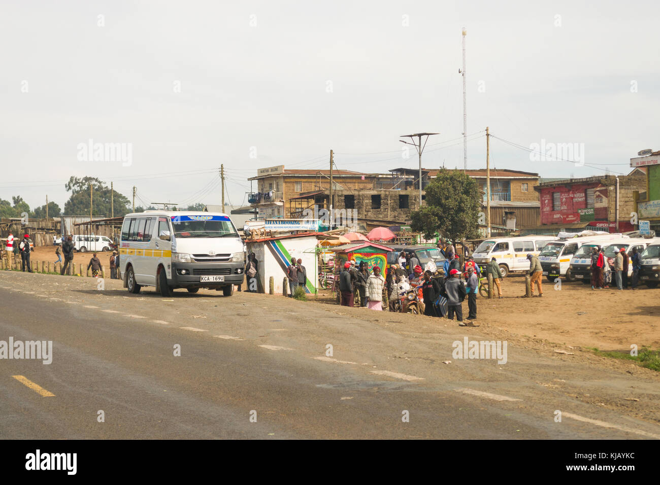 Una piccola città fermata bus con persone in attesa sul ciglio della strada come un matatu minibus arriva, Kenya, Africa orientale Foto Stock