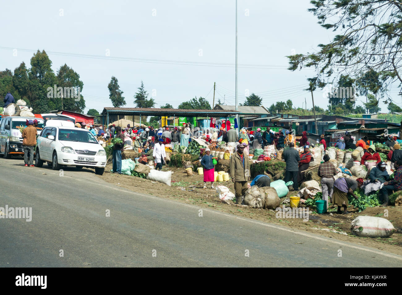 Un affollato mercato di fortuna nella piccola città lungo la strada con produrre sul display e persone camminare, Kenya, Africa orientale Foto Stock