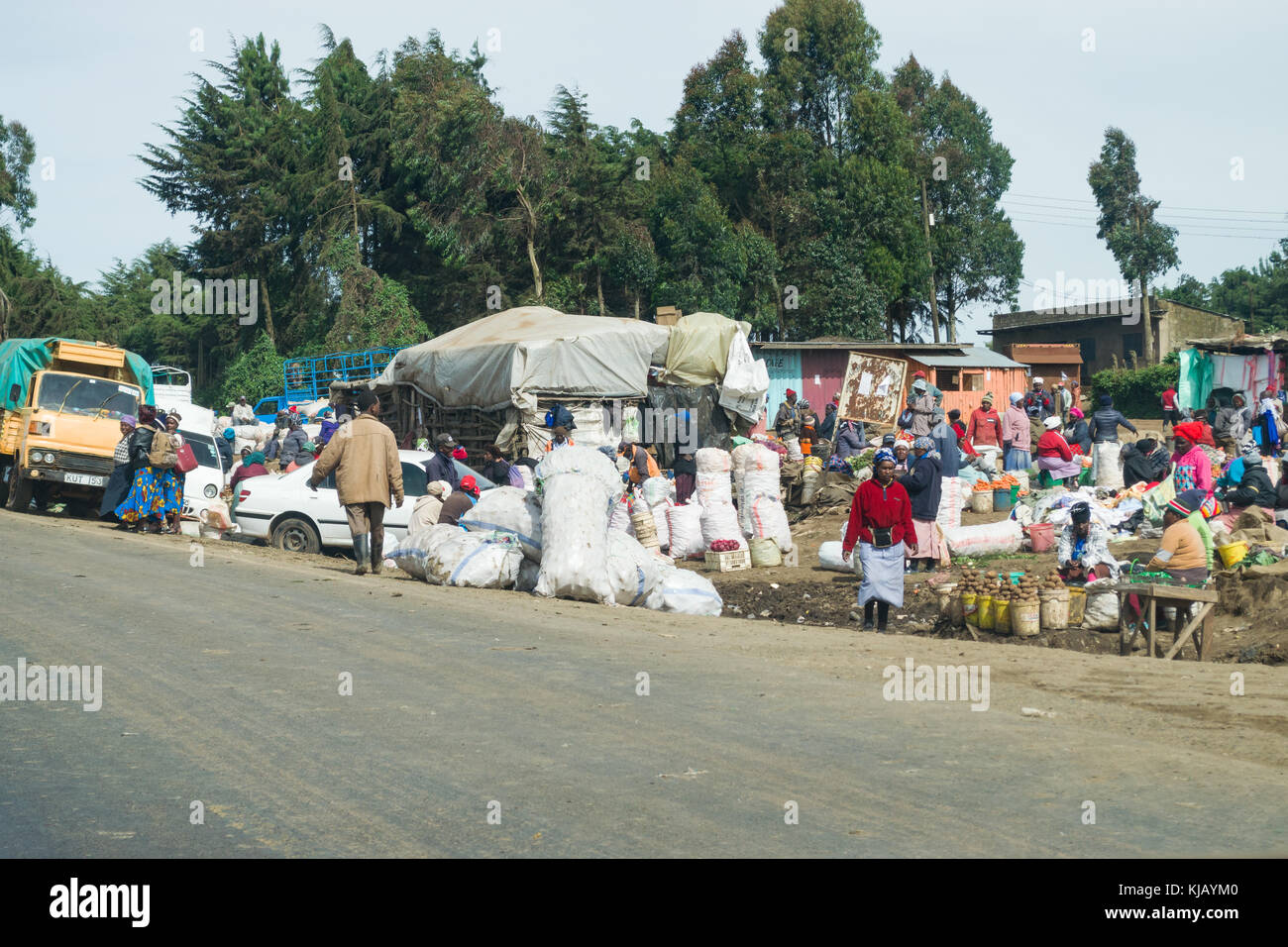 Un affollato mercato di fortuna nella piccola città lungo la strada con produrre sul display e persone camminare, Kenya, Africa orientale Foto Stock