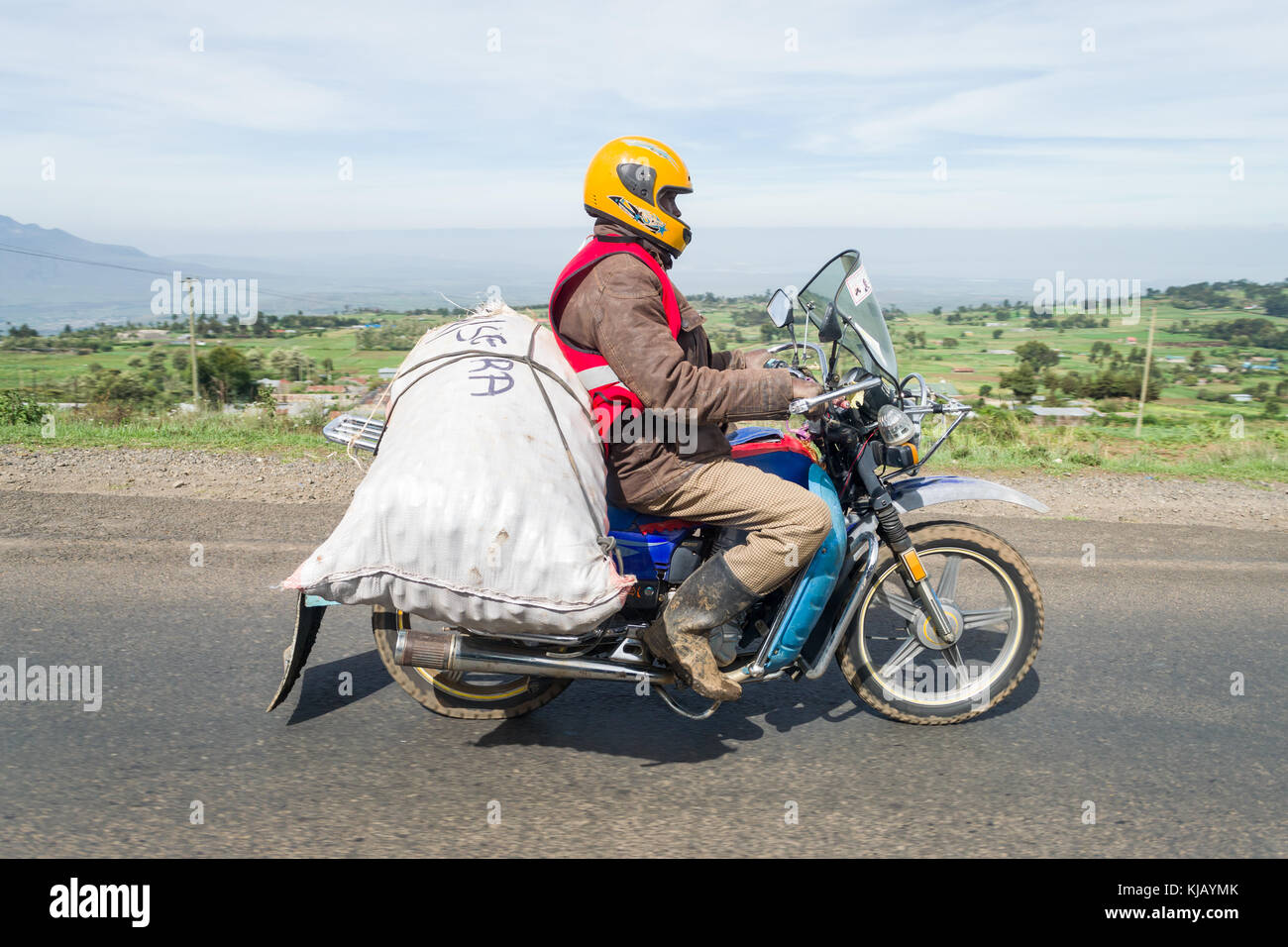 Un africano uomo alla guida di una moto con un sacco di grandi dimensioni delle merci assicurate al retro, Kenya, Africa orientale Foto Stock