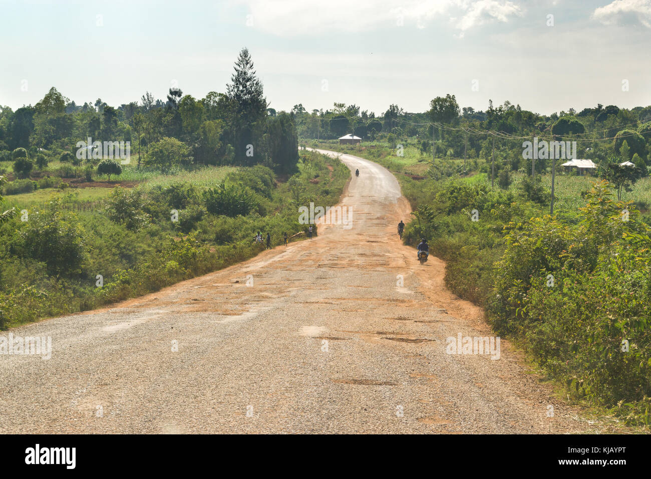 Una strada piena di buche con la gente che camminava sul ciglio della strada, Kenya, Africa orientale Foto Stock