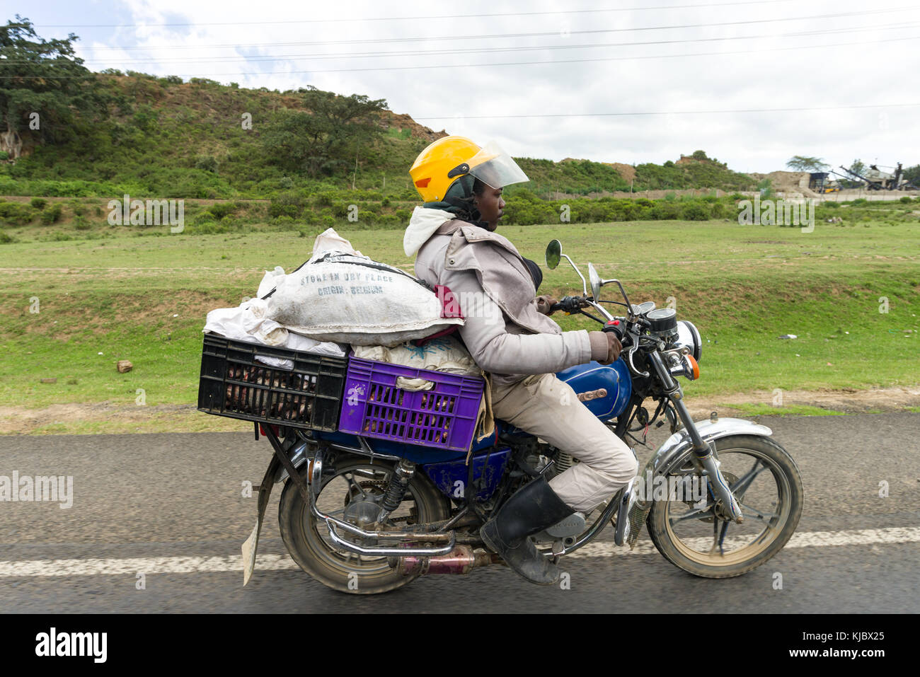 Un africano uomo si siede goffamente su una moto come egli trasporta una grande quantità di merci sul retro, Kenya, Africa orientale Foto Stock