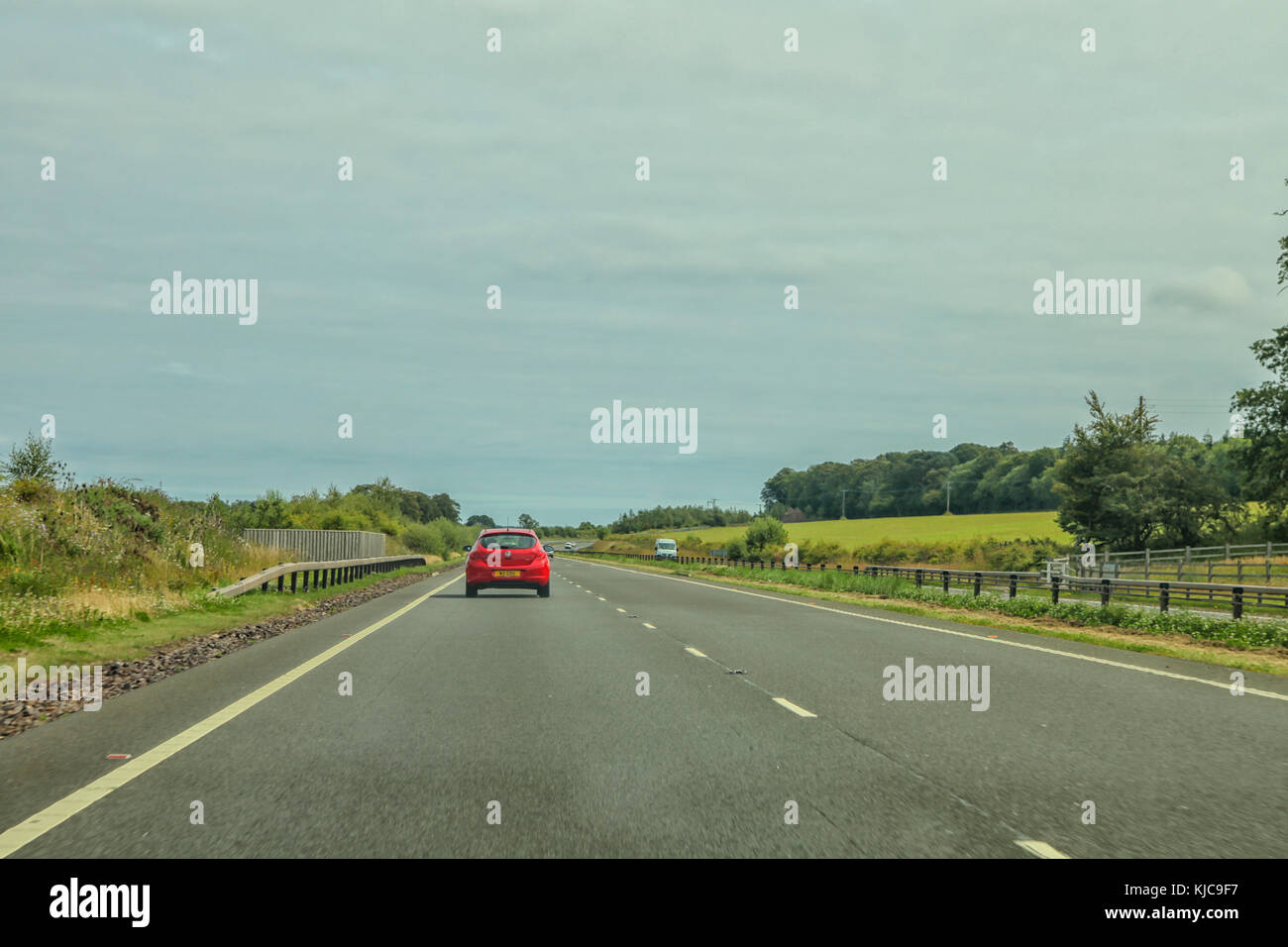 Auto rossa la guida sul lato sinistro di una tranquilla autostrada Foto Stock