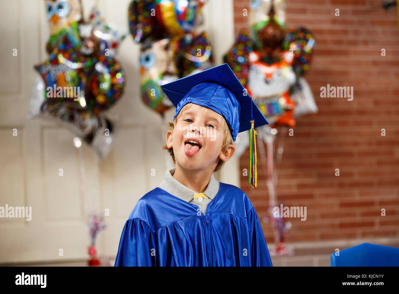 Ragazzo caucasico graduazione da indossare accappatoio con la lingua fuori Foto Stock