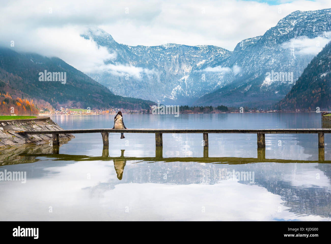 Donna seduta su un ponte di legno sopra il lago hallstatter, ammirando le cime delle alpi austriache e il loro riflesso nell'acqua, di hallstatt Foto Stock