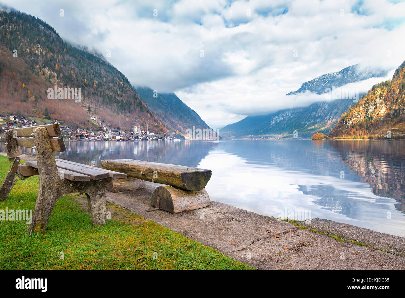 Destinazioni di viaggio Tema immagine con le montagne del Dachstein riflessi nell'acqua del lago hallstatter e panchine di legno sulla sua riva. Foto Stock