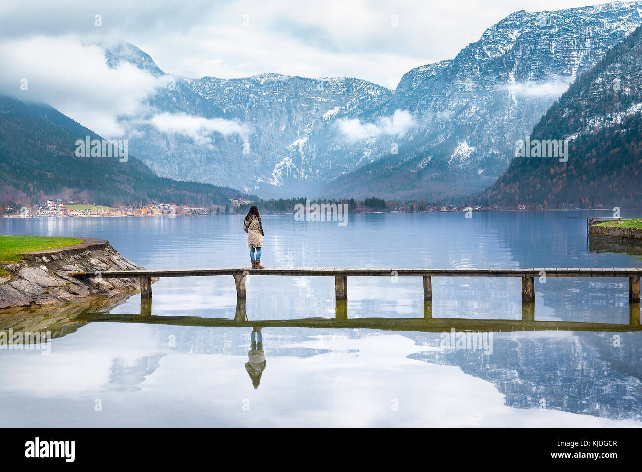 Giovane donna in piedi su un ponte di legno sopra il lago hallstatter godendo la vista delle Alpi austriache montagne riflesse nel lago d acqua Foto Stock