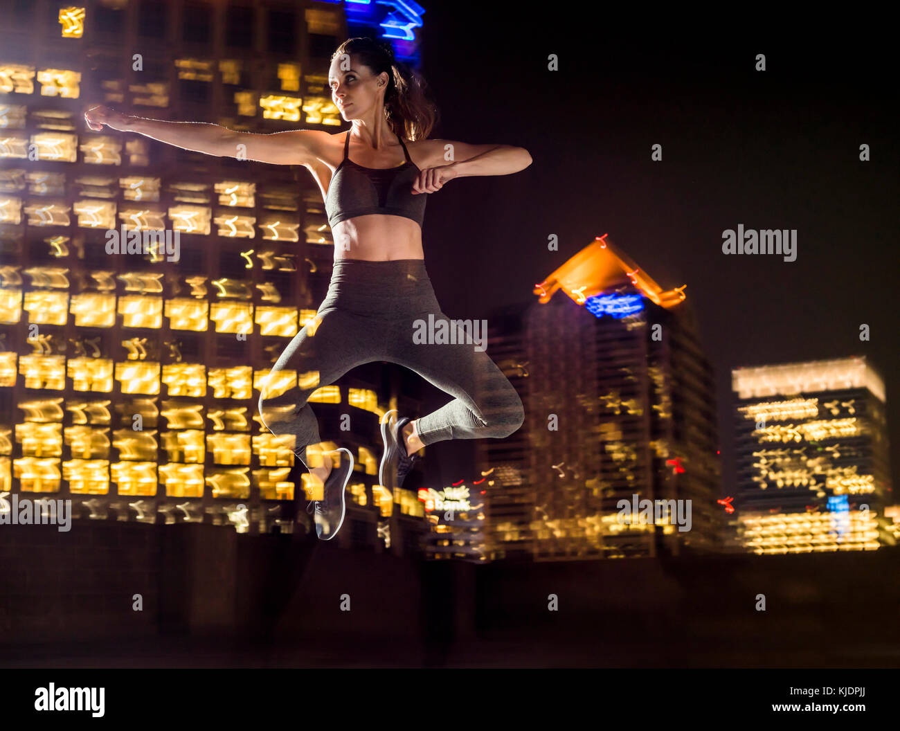 Doppia esposizione della donna caucasica jumping in città di notte Foto Stock