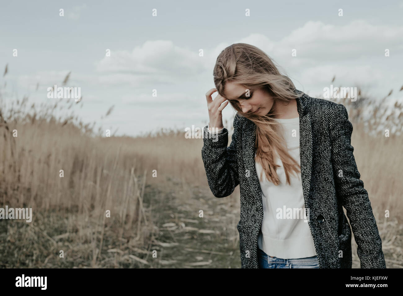 Donna con capelli lunghi biondi, ampia sopracciglia e con battenti capelli coperto il suo viso carino camminando sulla strada di campagna e guardando verso il basso . Ragazza capelli di regolazione Foto Stock