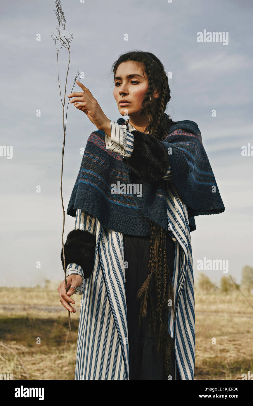 La donna caucasica indossando abiti tradizionali esaminando ramoscello Foto Stock