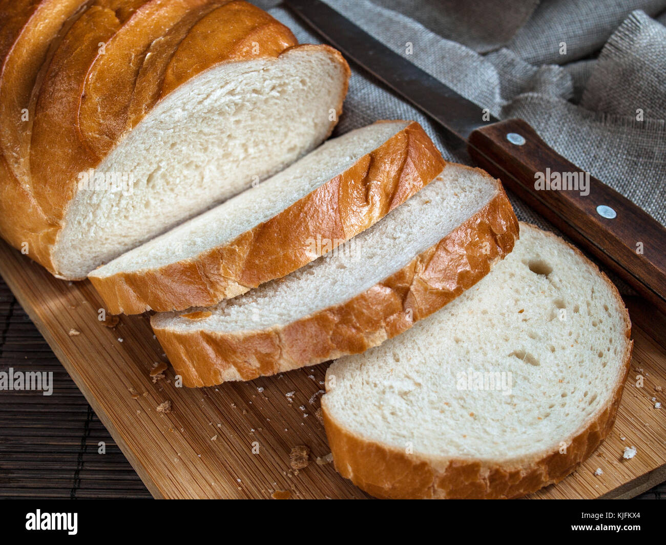Fresca e deliziosa, aromatico e appetitoso il pane bianco di farina di grano per la prima colazione, il pranzo e la cena pronta da mangiare tagliato a pezzi in una cucina in legno b Foto Stock