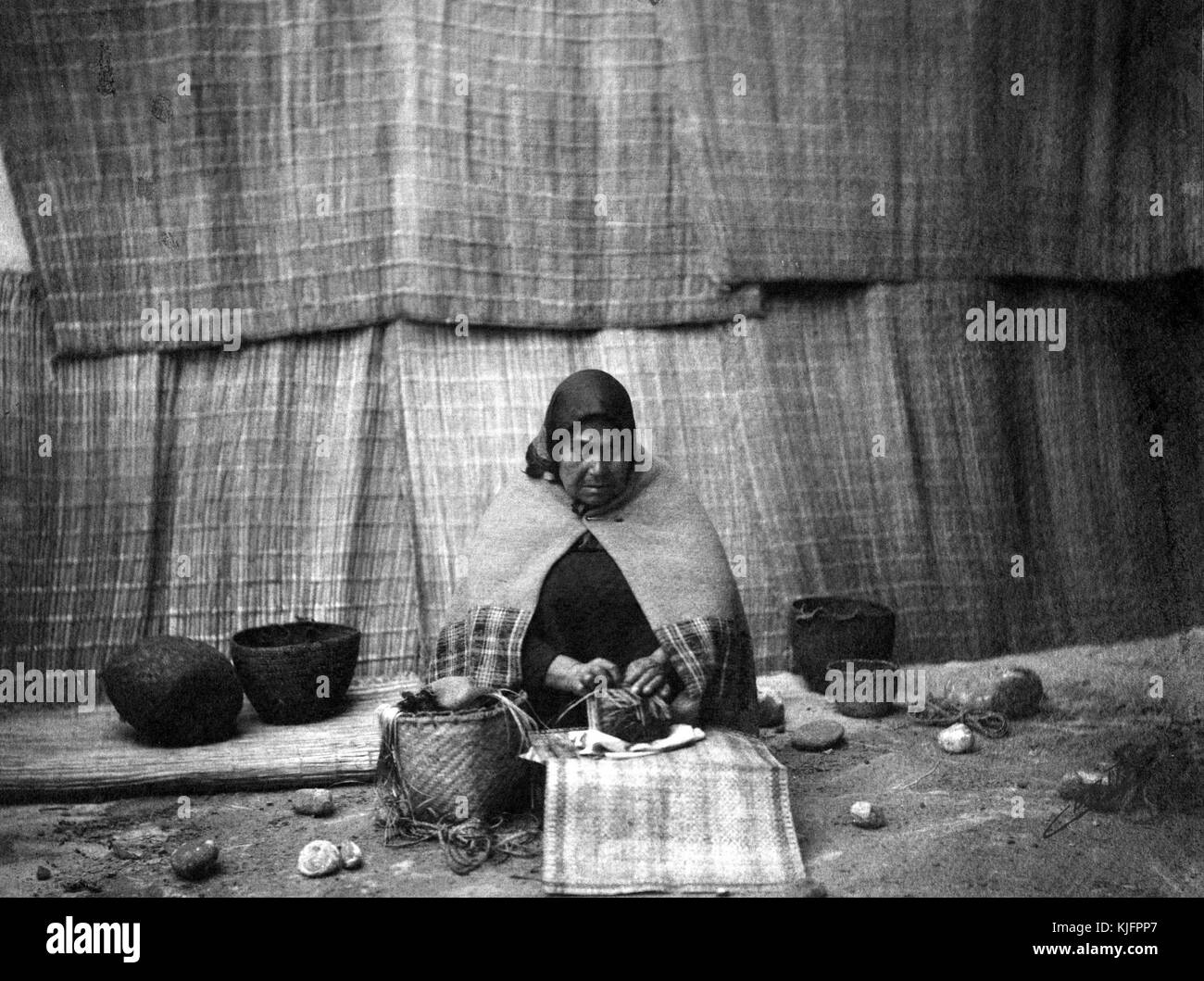 Fotografia, stampa platino, di una donna nativa americana, seduta a terra, tessendo un cesto, di Edward S Curtis, 1899. Dalla Biblioteca pubblica di New York. Foto Stock