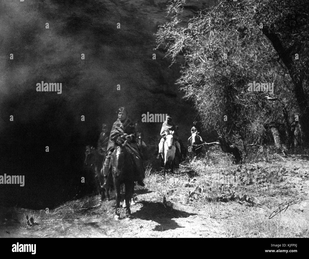 Fotografia di un gruppo di nativi americani che cavalcano i cavalli nel deserto, intitolata "Out of the Darkness, Navajo Indians Emerging from the shadow of the high walls of the Canyon de Chelly, Arizona", di Edward S Curtis, Arizona, 1904. Dalla New York Public Library. Foto Stock
