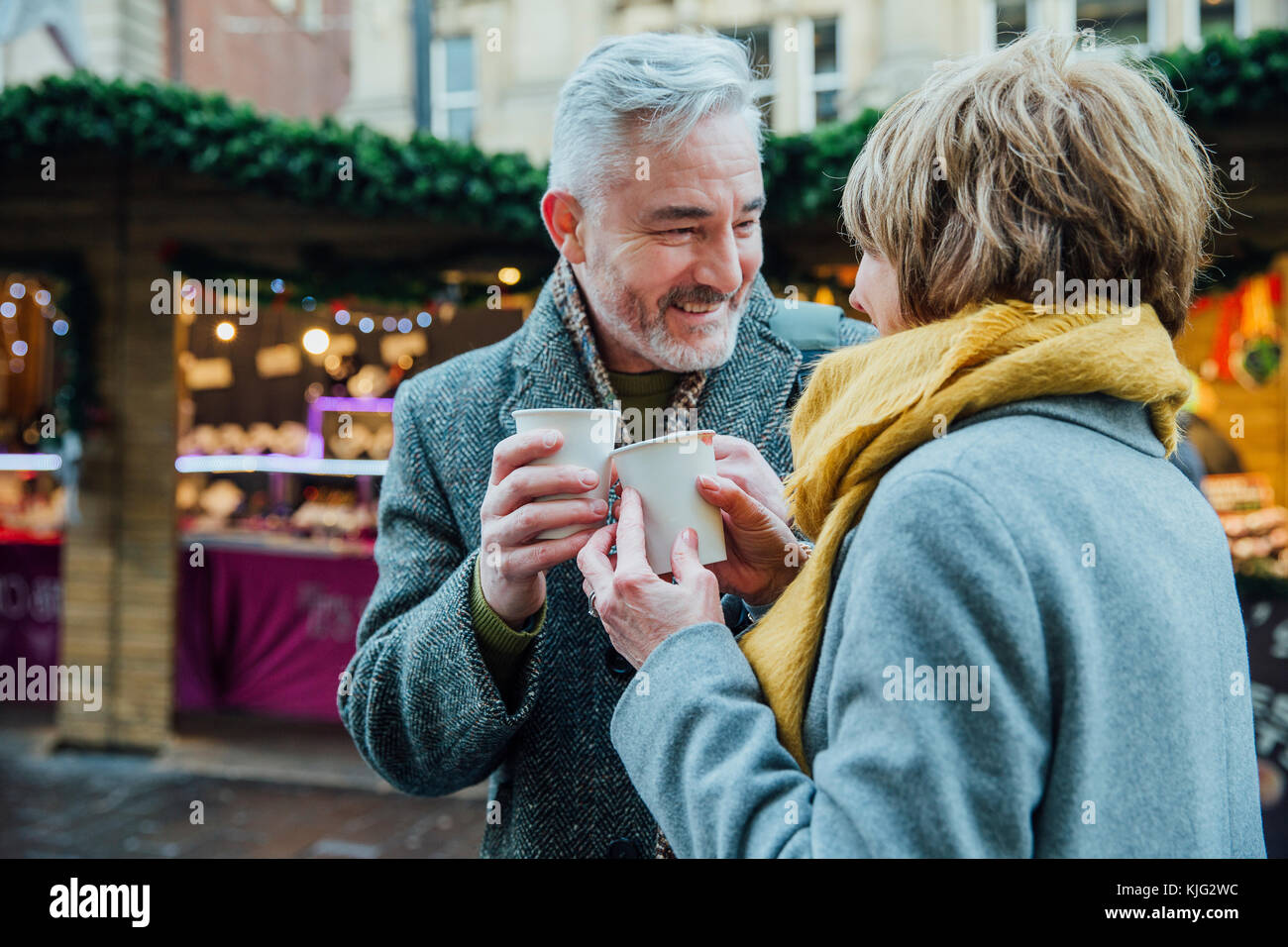 Coppia matura sono bere bevande calde in una città mercato di Natale. Essi sono la tostatura le tazze monouso. Foto Stock