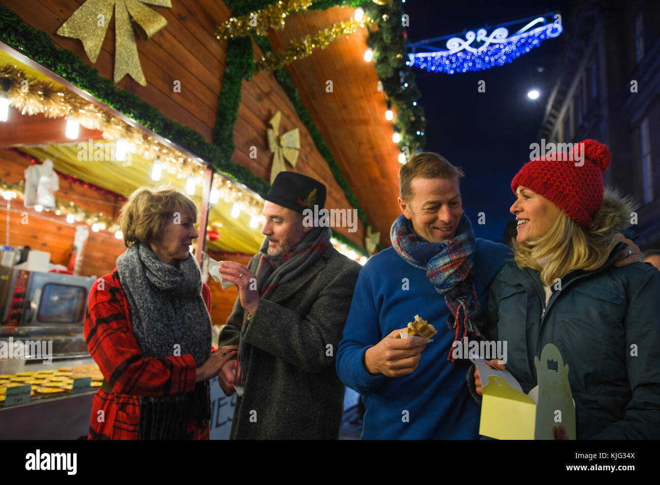 Coppie mature sono ad un mercatino di Natale in città. Essi sono la condivisione di cialde dolci che essi hanno acquistato da uno degli stalli. Foto Stock