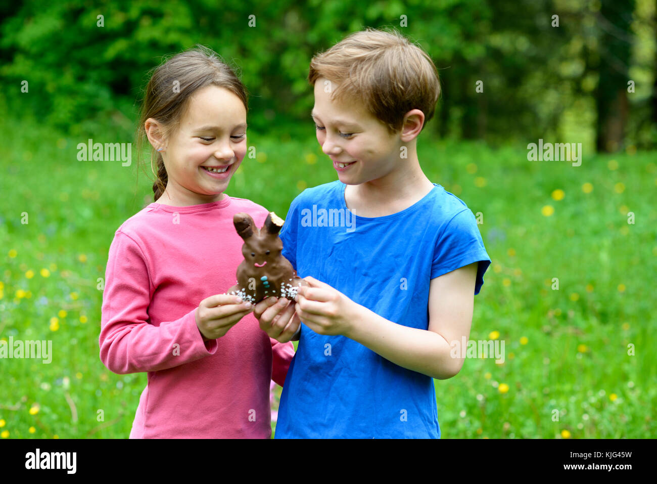 Junge und Mädchen, Geschwister beißen in einen Schokoladen Osterhasen, Ostern, Bayern, Deutschland Foto Stock