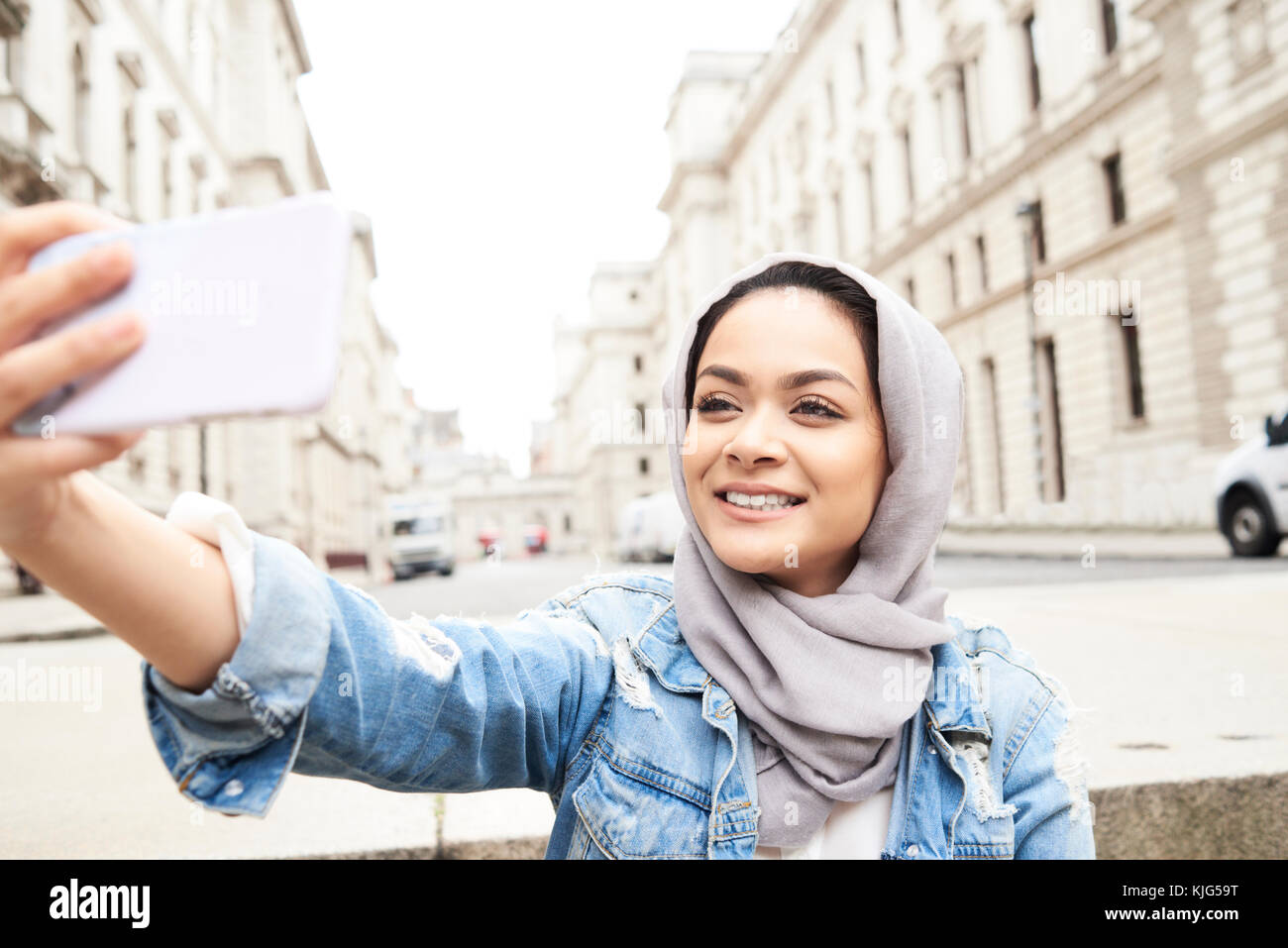 Londra, UK, Inghilterra, giovane bella ragazza musulmana prendendo un autoritratto con il suo telefono indossando il hijab grigio, musulmana studente universitario Foto Stock