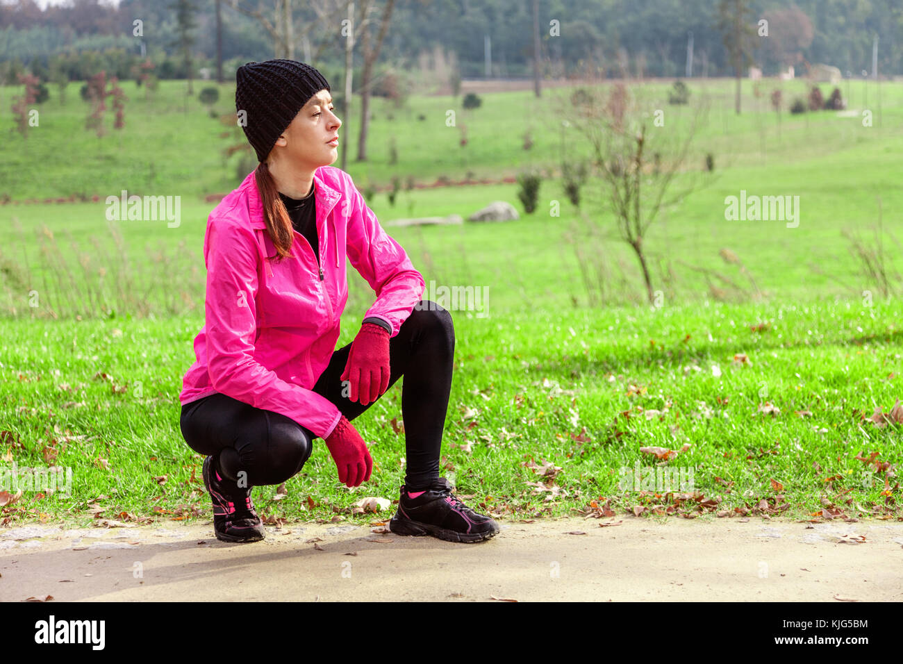 Giovane donna analizzando la traccia prima di eseguire in una fredda giornata invernale sulla via della formazione di un parco urbano. atleta femminile indossando giacca a vento rosa, b Foto Stock
