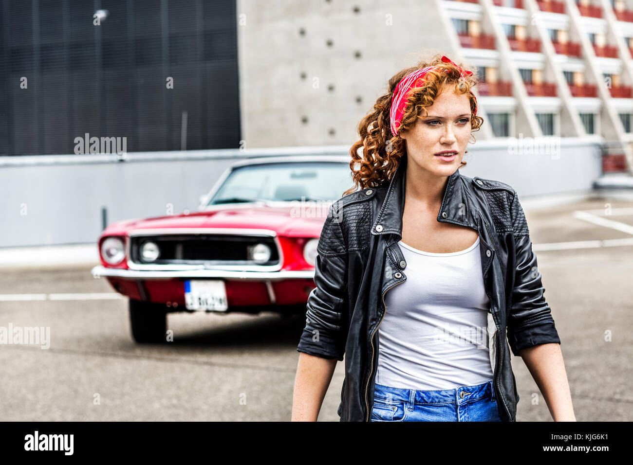 Redheaded donna accanto alla vettura sportiva sul livello di parcheggio Foto Stock