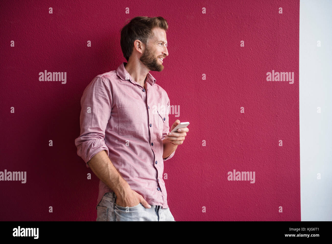 Uomo in piedi contro il muro viola azienda telefono cellulare Foto Stock