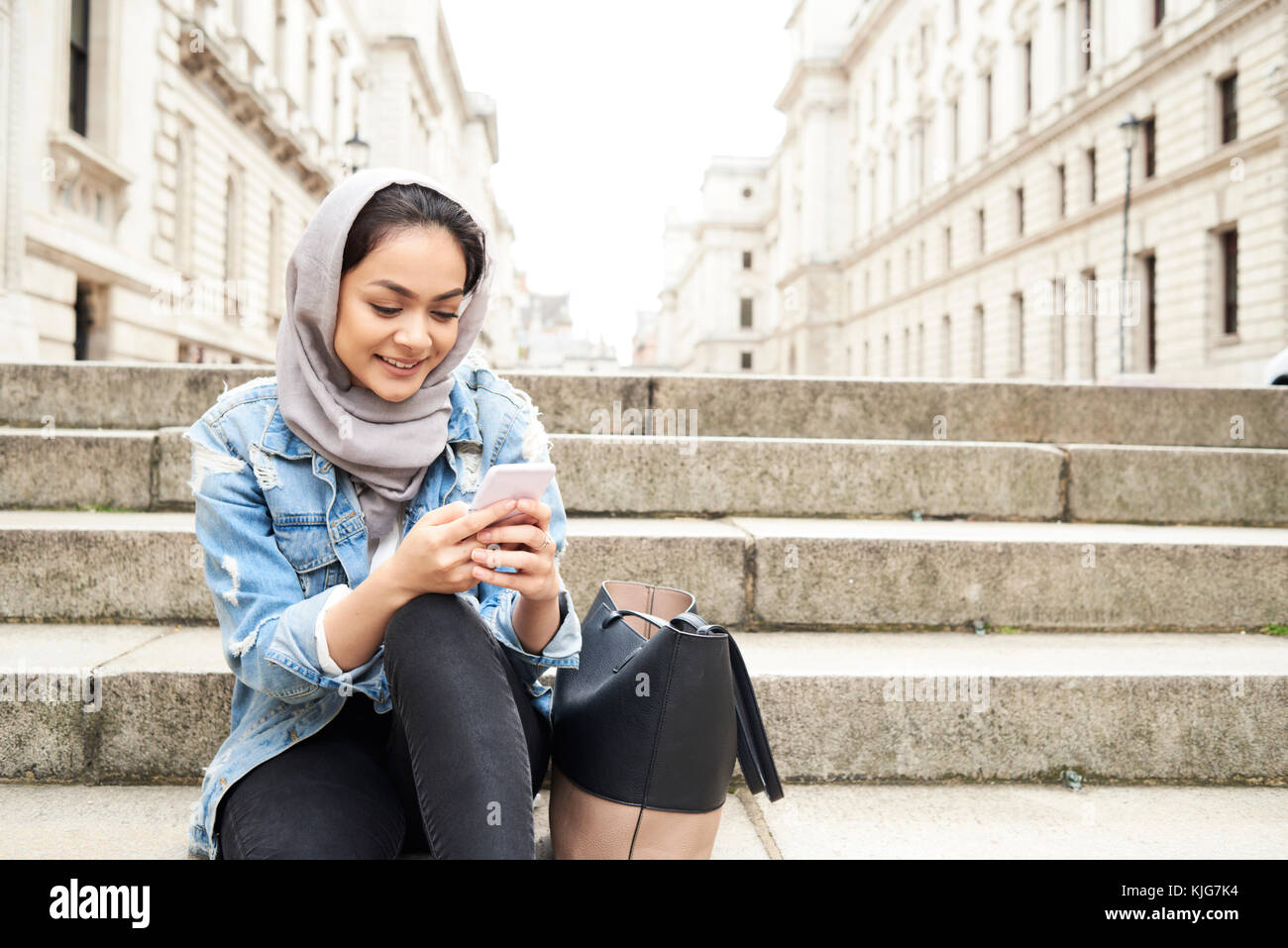 Londra, UK, Inghilterra, graziosa ragazza musulmana in chat tramite il telefono indossando il hijab in strada, musulmana studente universitario Foto Stock