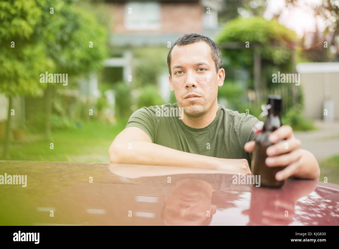 Ritratto di grave uomo con bottiglia di birra appoggiata sul tetto del veicolo Foto Stock