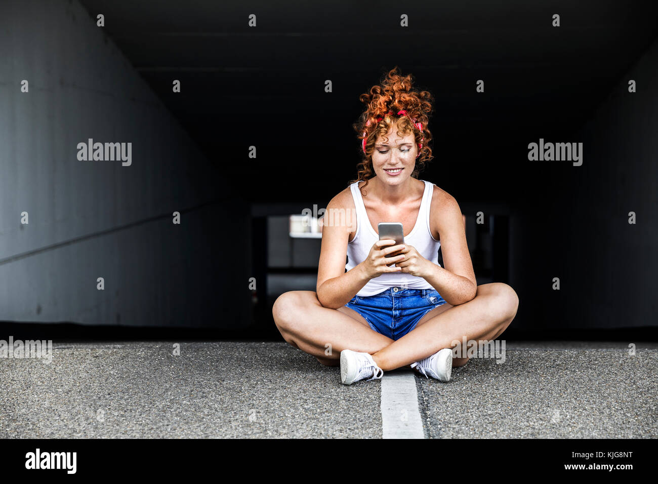 Redheaded donna seduta sul parcheggio livello azienda telefono cellulare Foto Stock