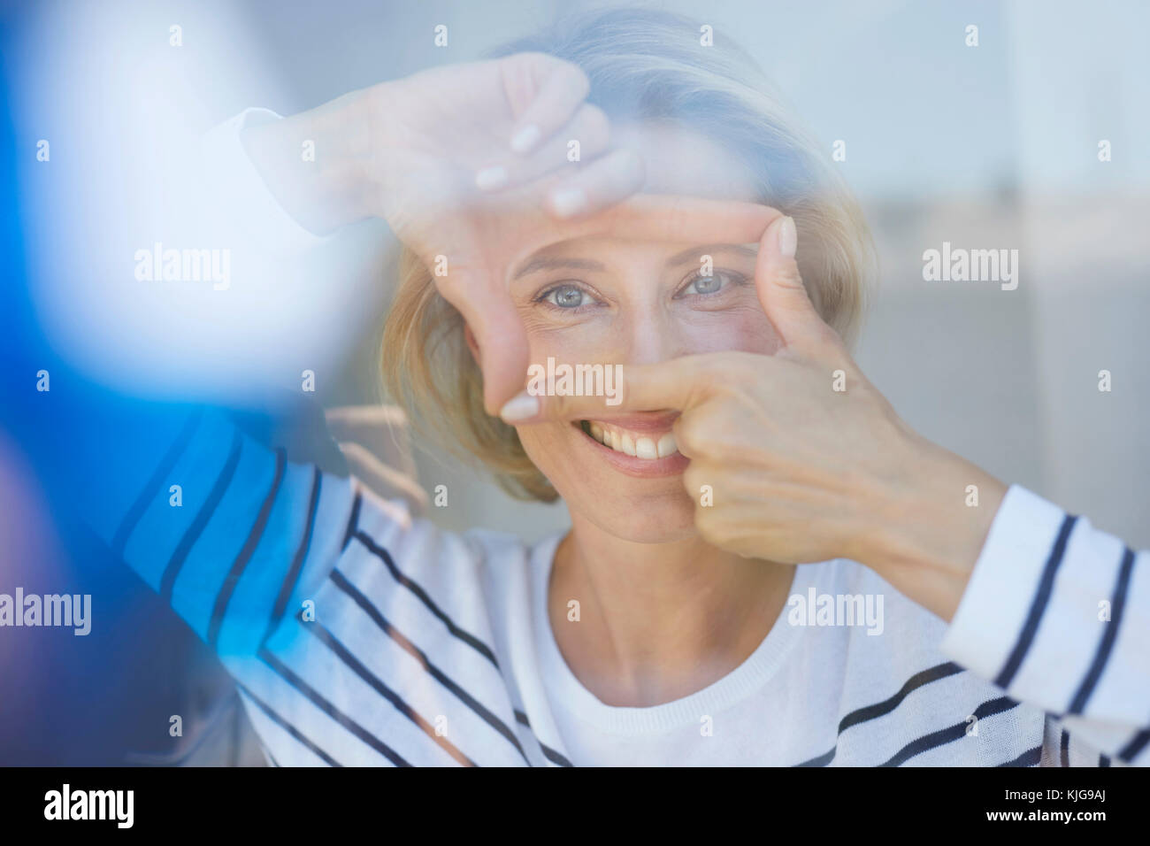 Ritratto di ridere donna bionda la costruzione di telaio con le dita mentre guardando viewer Foto Stock