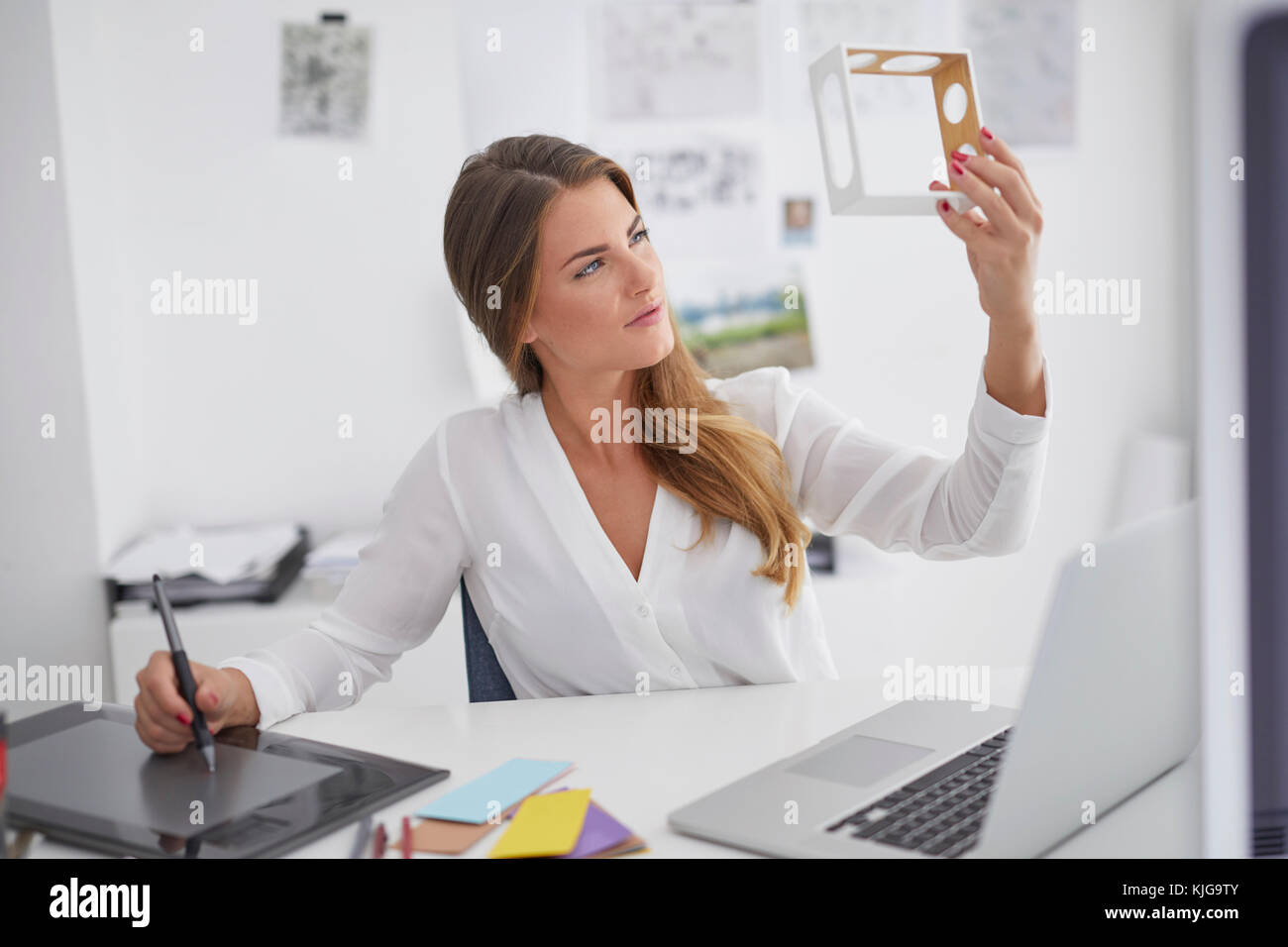 Giovane donna alla scrivania in ufficio modello di contenimento e con tavoletta grafica Foto Stock