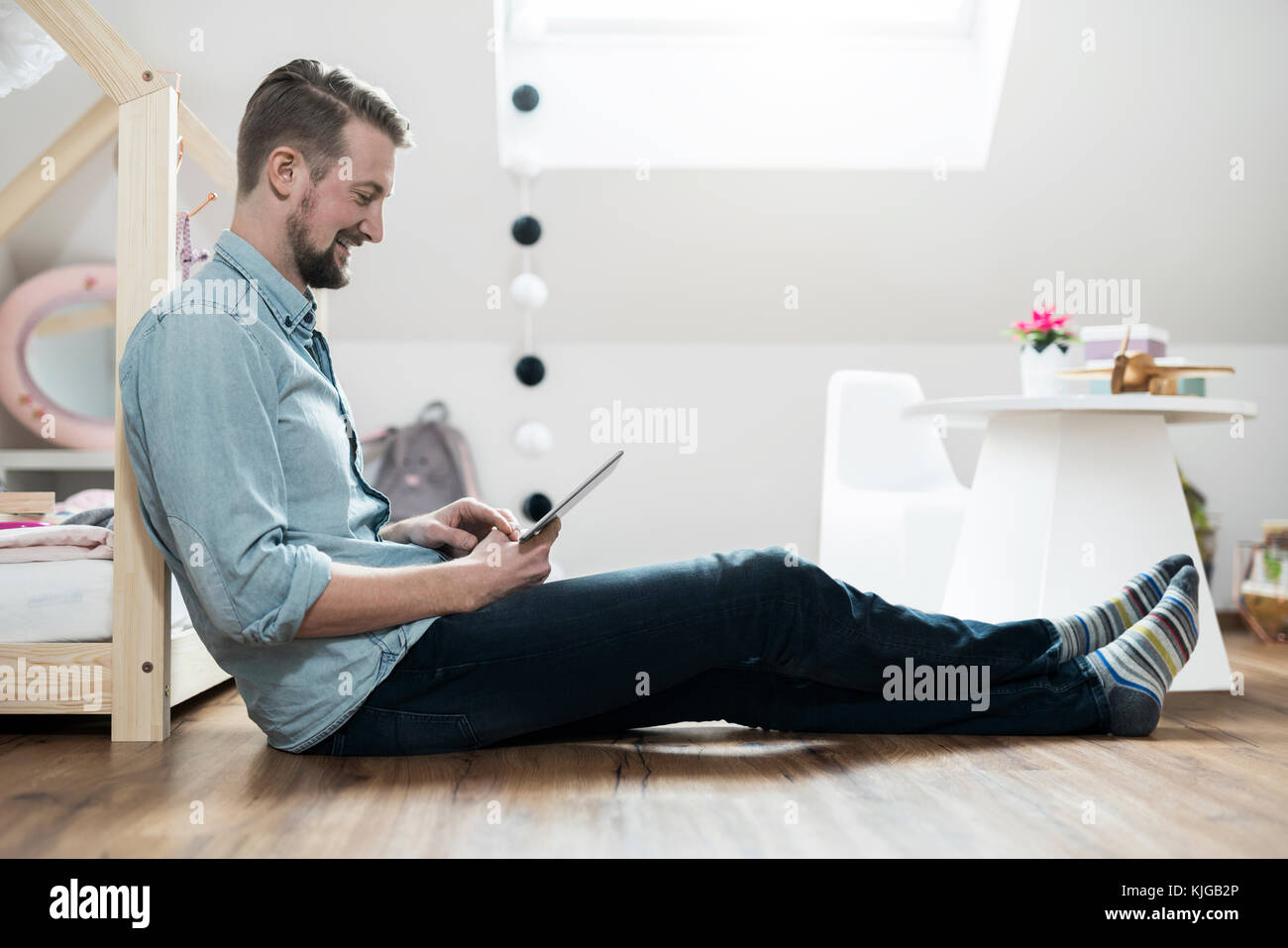 Padre seduto sul pavimento in vivaio guardando tablet Foto Stock