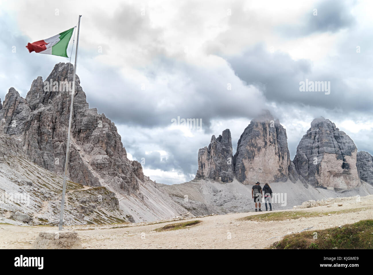 Bandiera italiana e due escursionisti in parte anteriore del Monte Paterno (paternkofel) e cloud-coperto tre cime di Lavaredo nelle Dolomiti Foto Stock