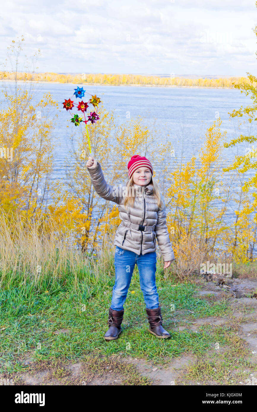 Ragazza con vento colorato giocattolo sul fiume sfondo in autunno Foto Stock