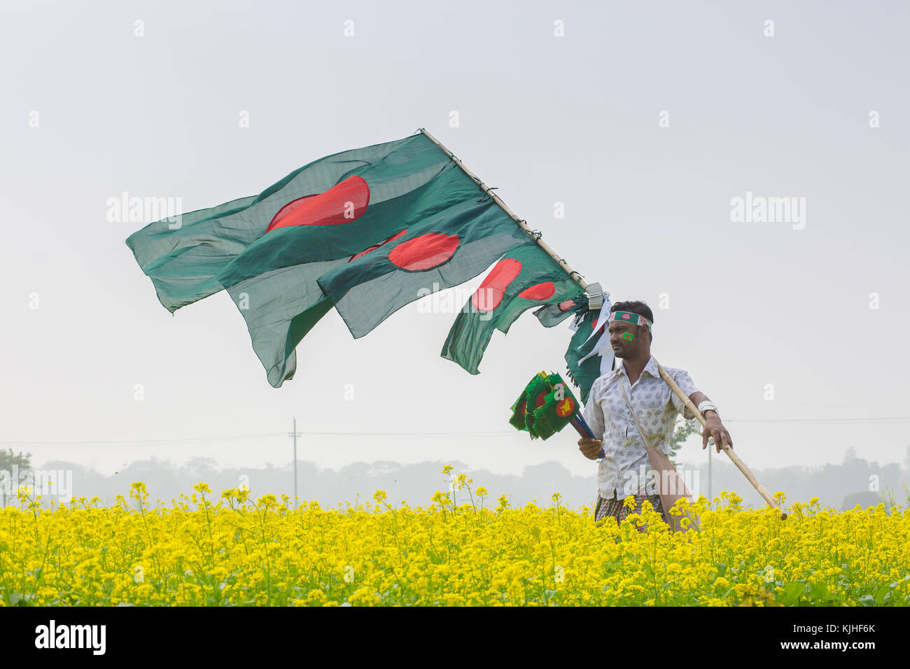 Un hawker bangladese vende bandiere nazionali in campo di senape in munshigonj, Dhaka, Bangladesh. Foto Stock