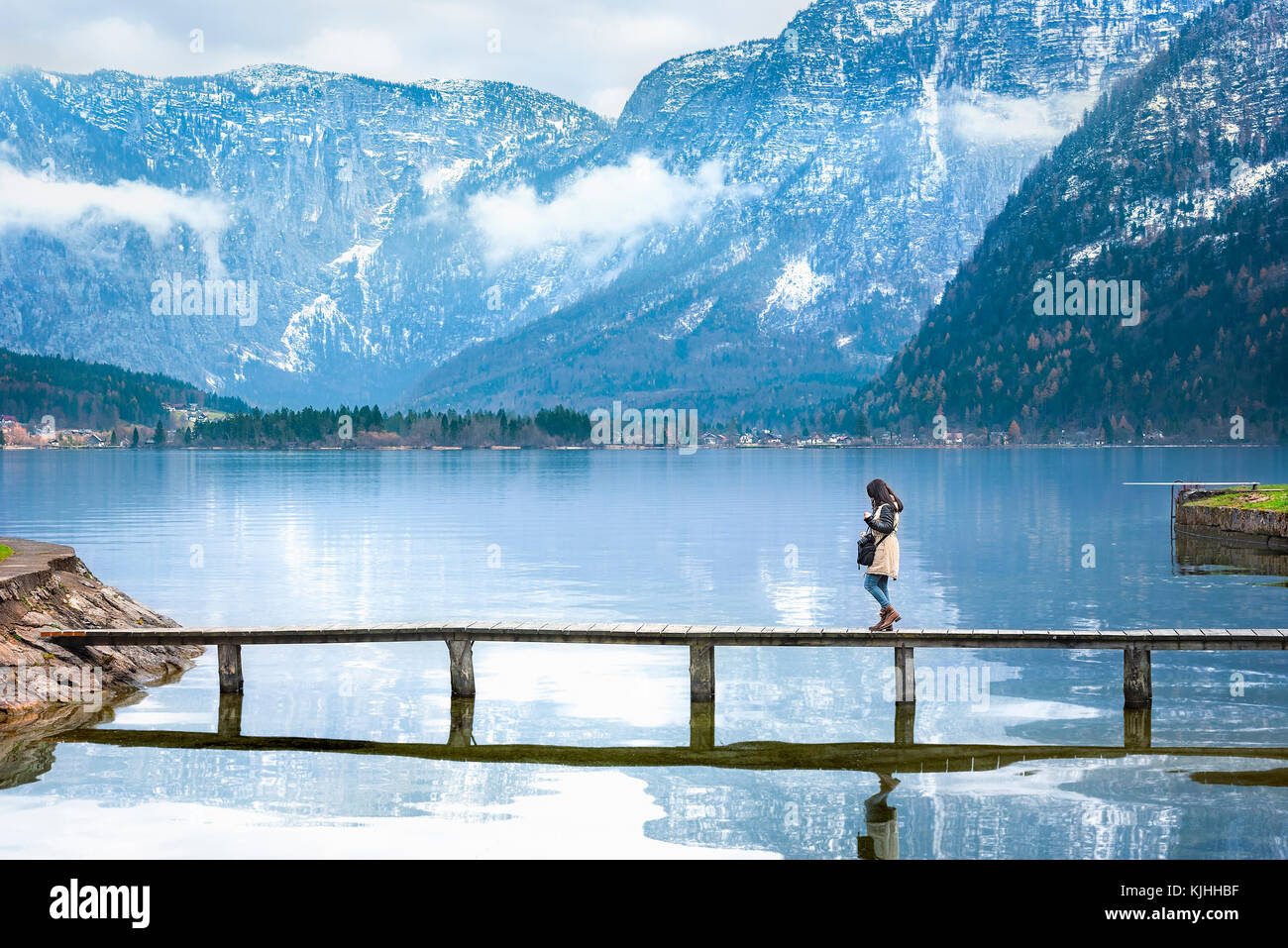 Destinazione di viaggio Tema immagine con una donna che cammina su uno stretto ponte che attraversa il lago hallstatter, circondata dalle Alpi austriache montagne. Foto Stock