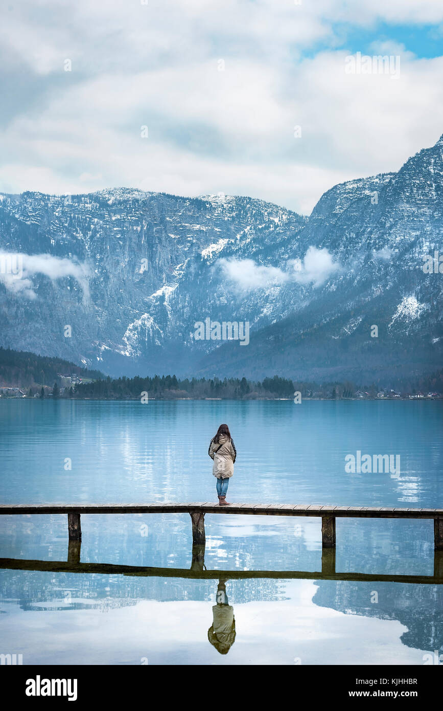 Percorsi di viaggio immagine con una donna in piedi su un ponte, ammirando il panorama delle Alpi austriache montagne, che si riflette nel lago hallstatter, Austria Foto Stock
