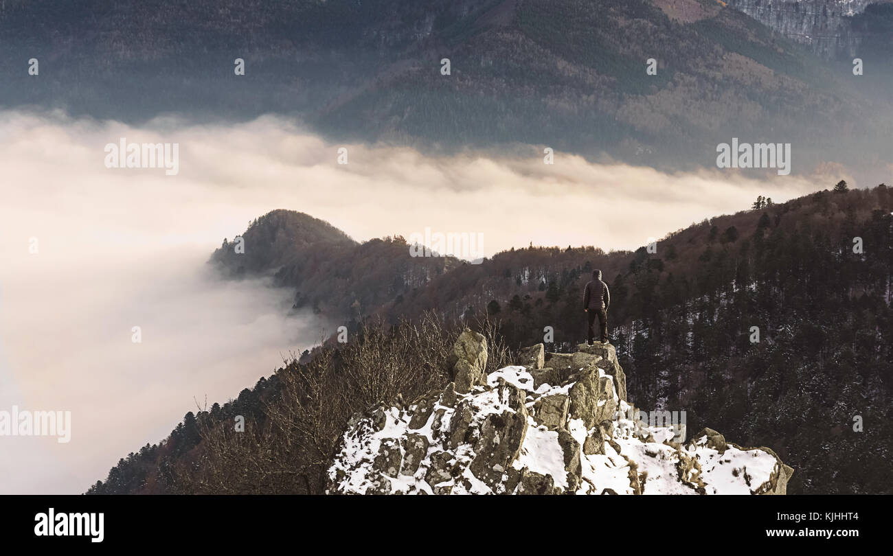 Un escursionista in piedi su un picco innevato, guardando una inversione di cloud in montagna all'inizio dell'inverno. Wanderlust nei Vosgi (Francia). Foto Stock