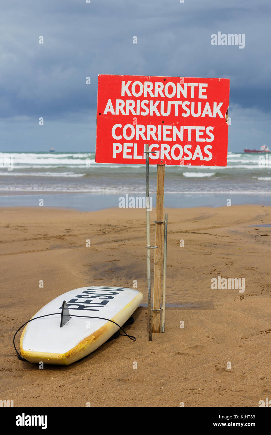 Tavola da surf e la pubblicità di pericolo di correnti pericolose in una spiaggia in un giorno di tempesta in paese basco Foto Stock