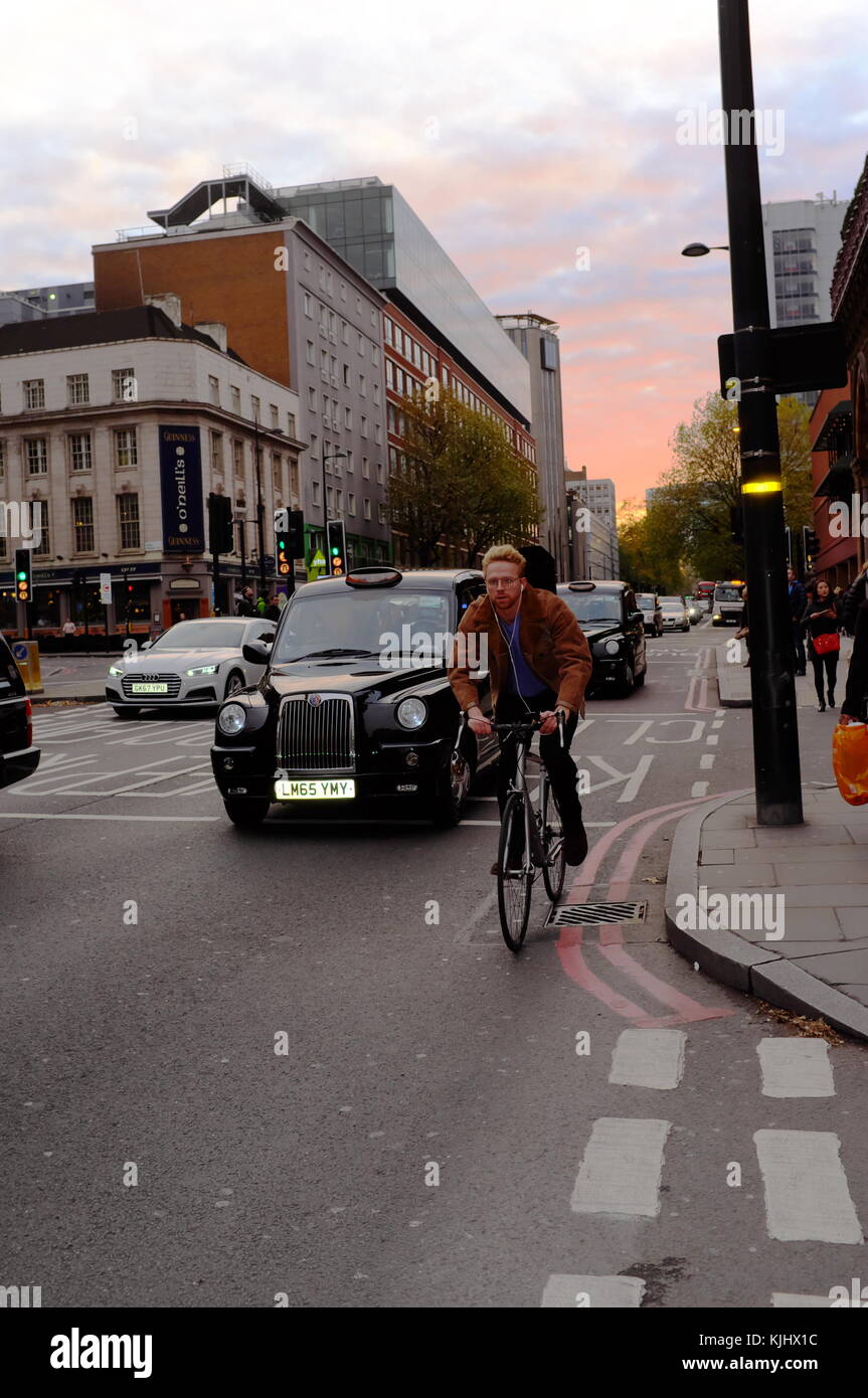 Giovane uomo passato in bicicletta i taxi neri di Londra, Inghilterra Foto Stock