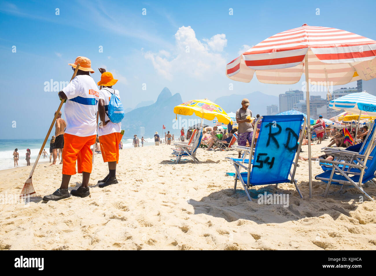 Rio de Janeiro - marzo 06, 2016: spiaggia pulitori su occupato Ipanema beach con ombrelloni e sedie con due fratelli montagne sullo sfondo. Foto Stock