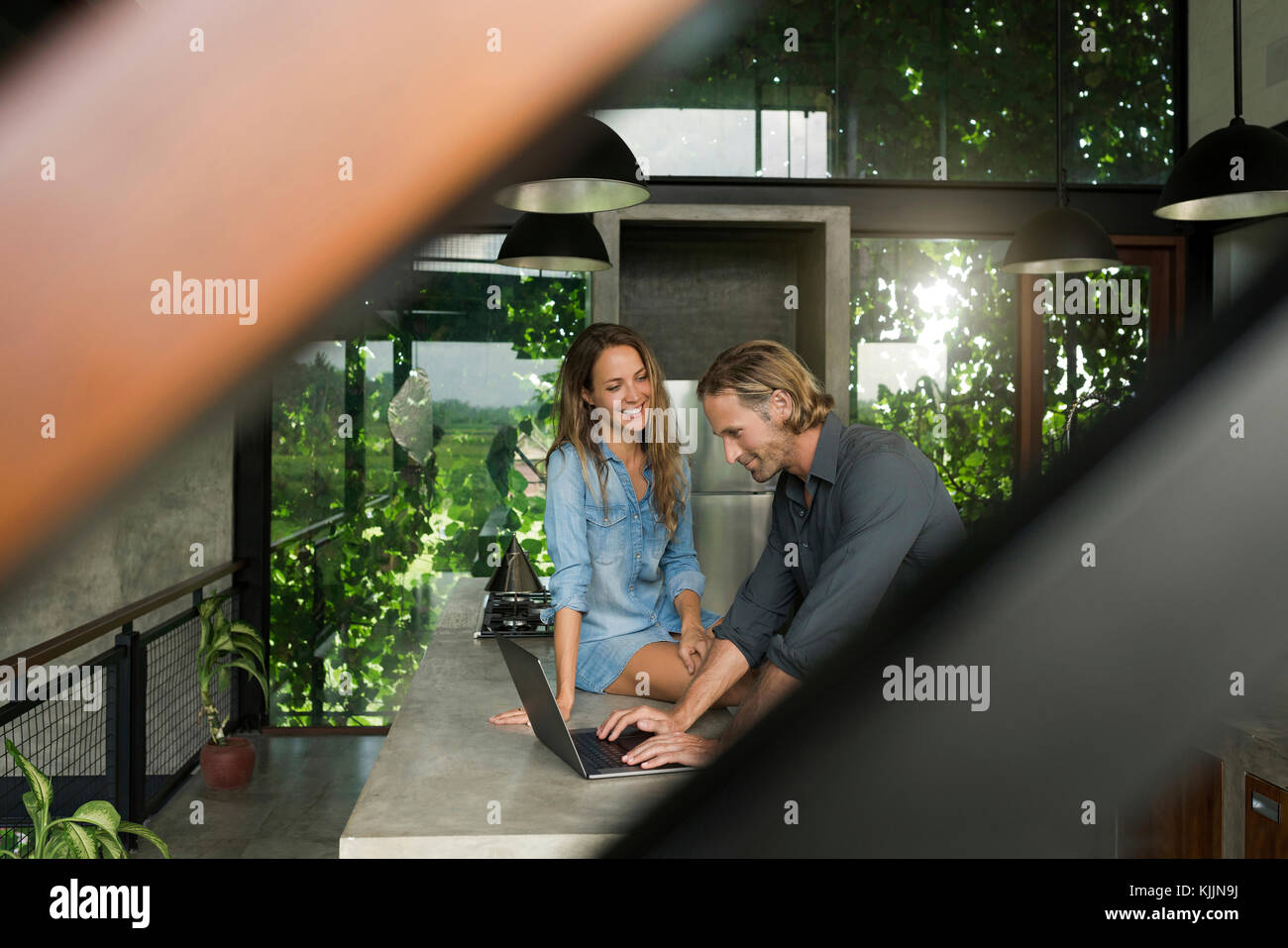 Donna sorridente al marito con il computer portatile in una moderna cucina minimalista nel design contemporaneo house Foto Stock