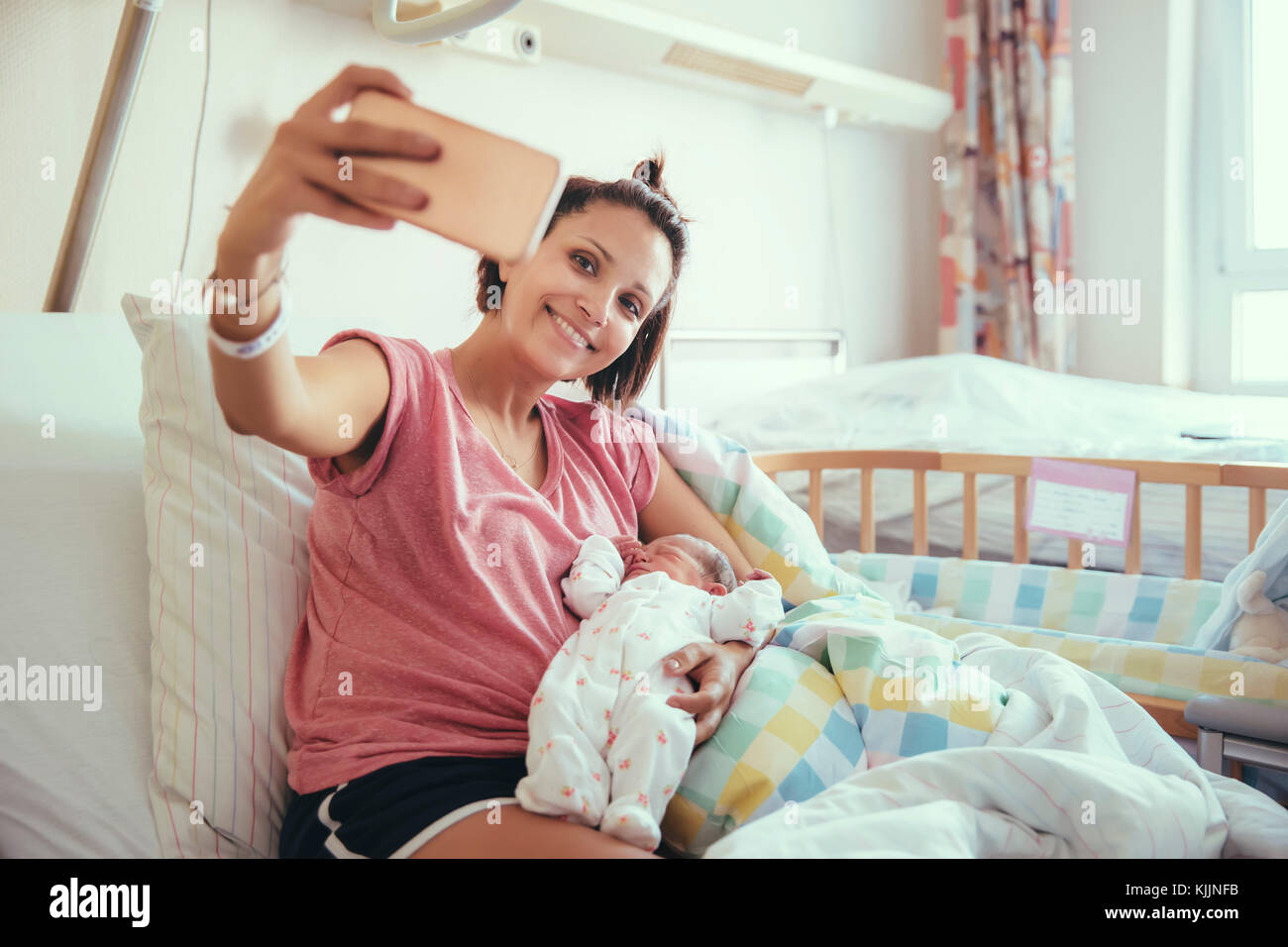 Madre prendendo un selfie con il suo neonato nel letto di ospedale Foto Stock