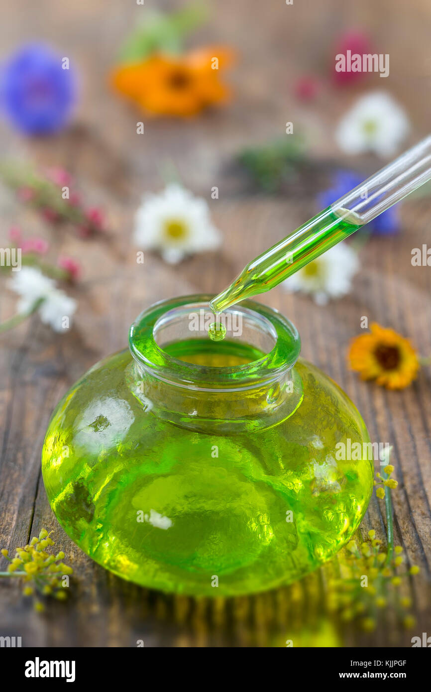 Trasparente bottiglie in vetro con gocce di liquido essenziale in contagocce su sfondo di legno con fiori di medicinali Foto Stock